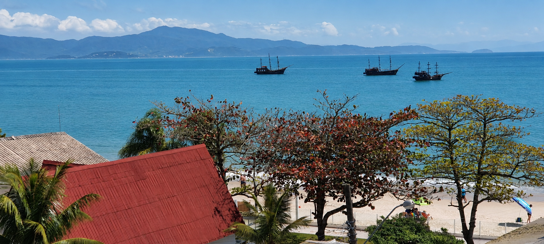 Vista de la playa de Cachoeira do Bom Jesus con veleros en el mar y morros al fondo