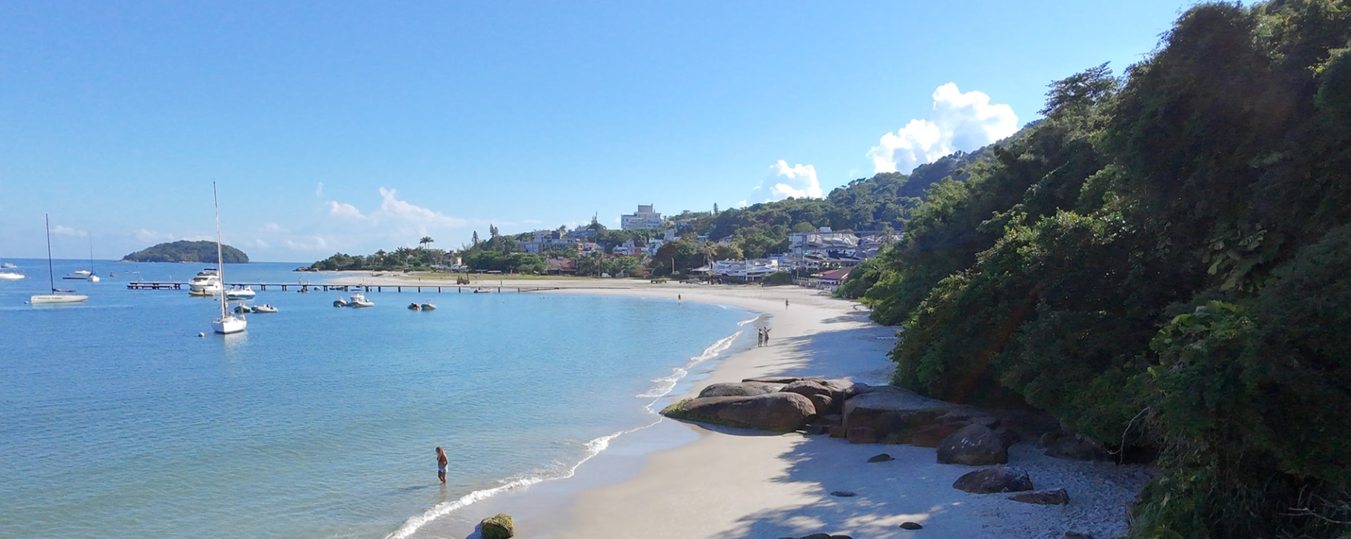 Playa de arena blanca con rocas, vegetación nativa y embarcaciones fondeadas