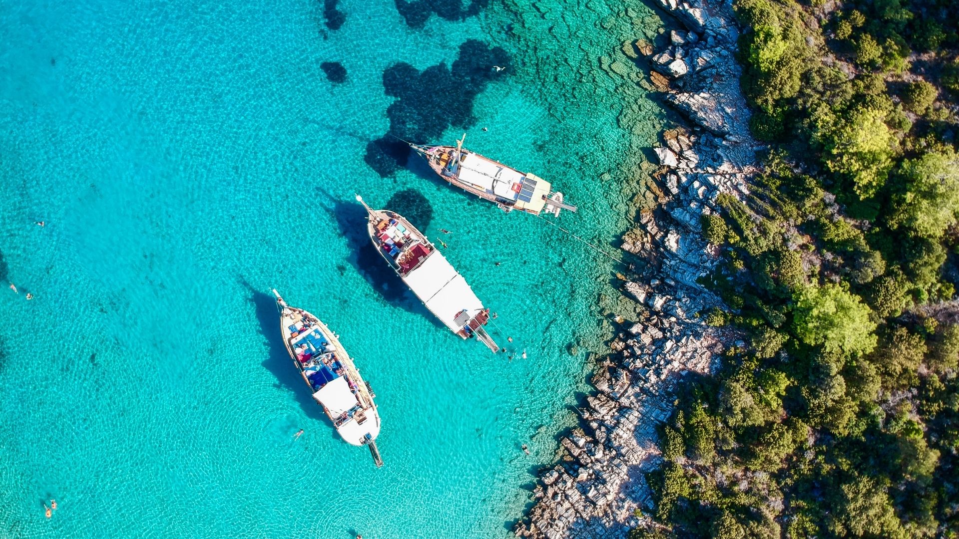 Vista aérea de veleros fondeados en agua turquesa junto a una costa rocosa y verde