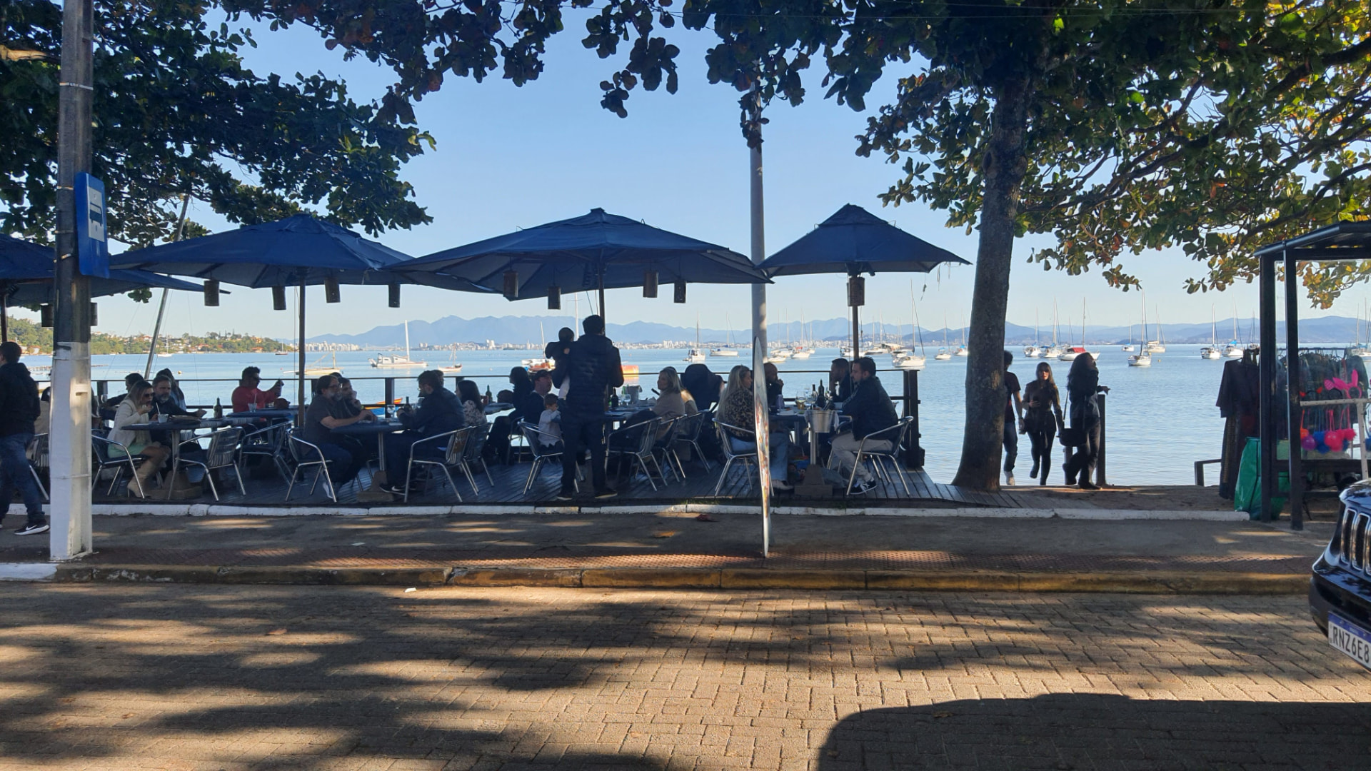 Terraza de restaurante frente a la bahía con veleros fondeados y sierra al fondo
