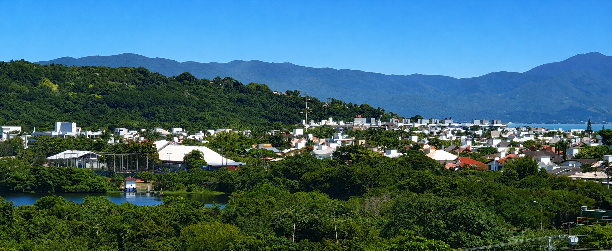 Vista de Jurerê con casas bajas entre vegetación, morro verde y bahía al fondo