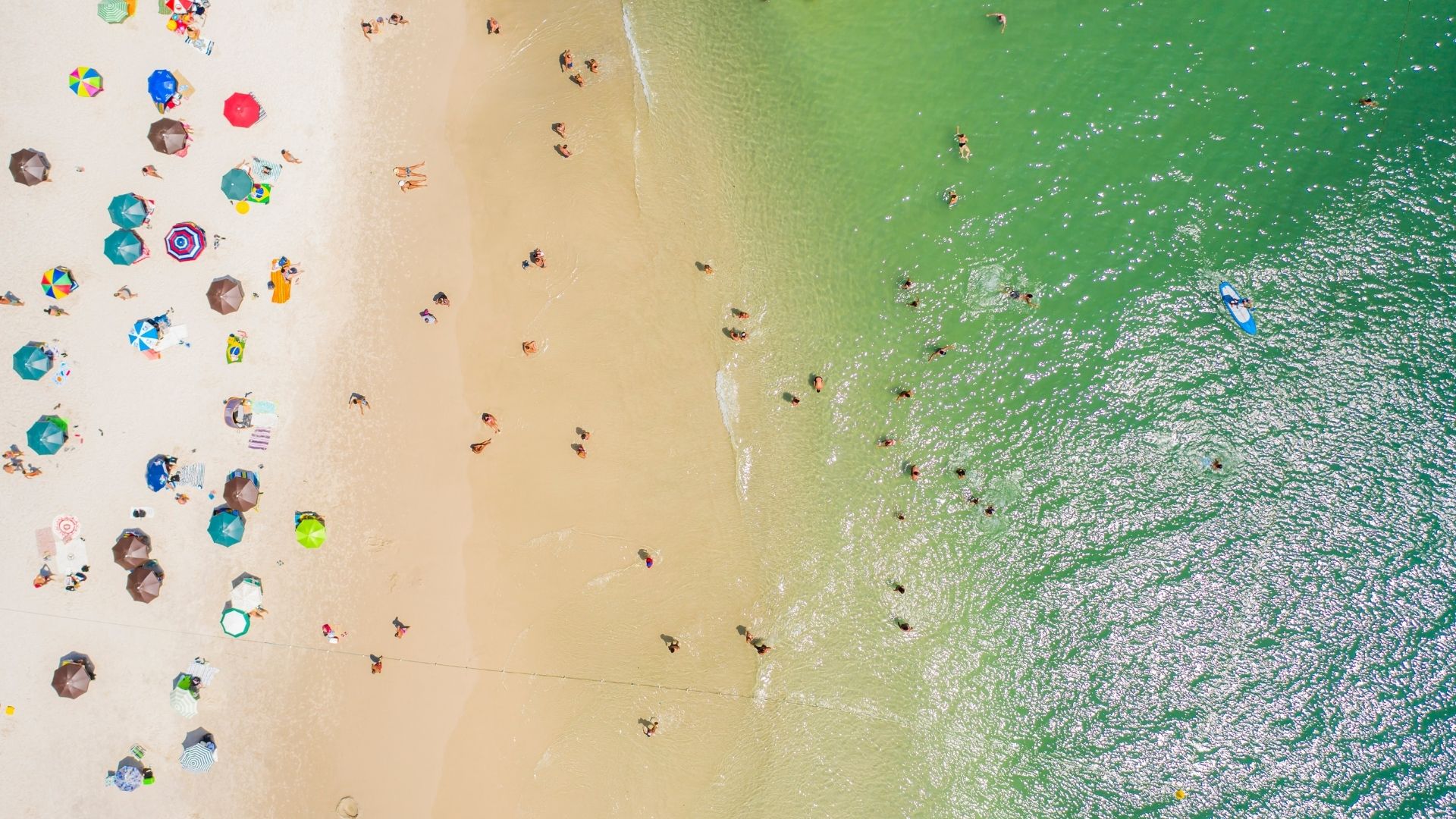 Vista aérea cenital de una playa con sombrillas, arena y agua verde turquesa