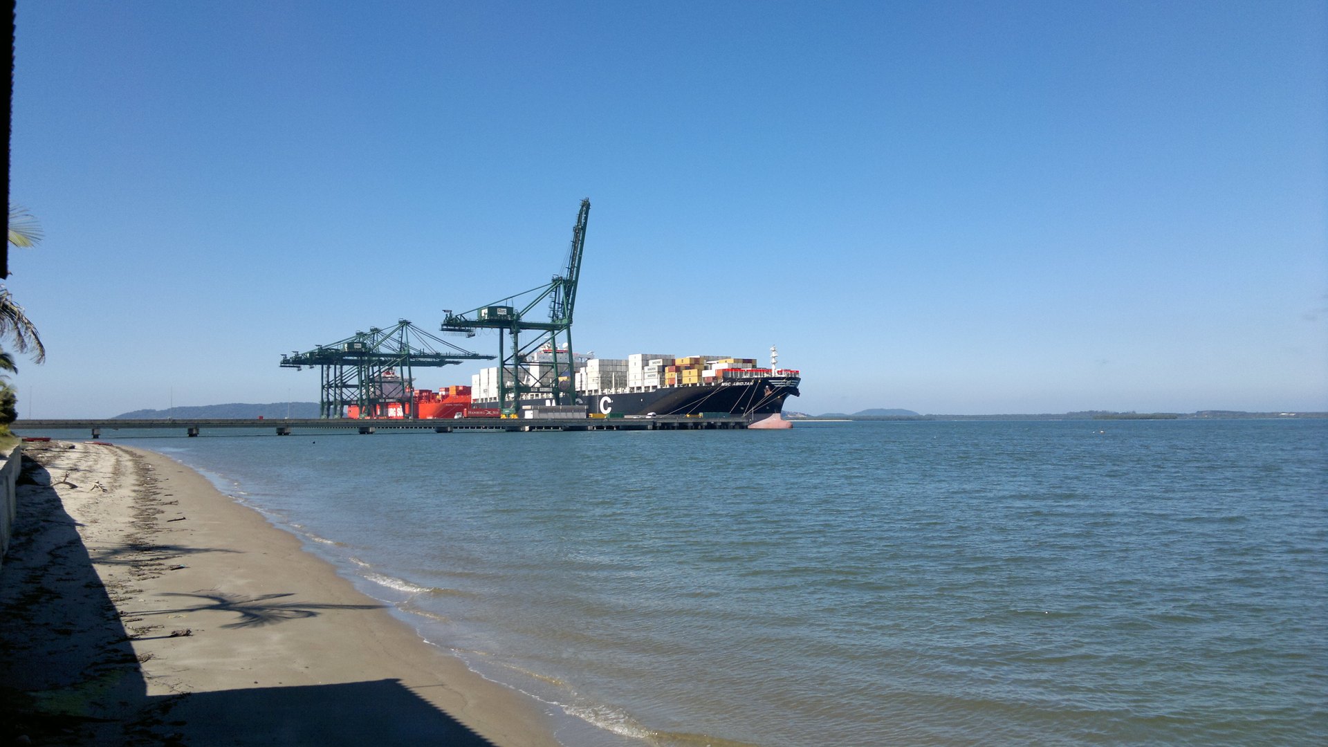 Terminal portuario de Itapoá visto desde la playa, con grúas y buque de contenedores