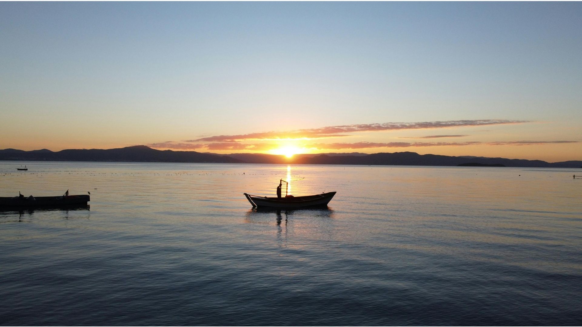 Pescador en su barca al atardecer sobre aguas calmas con morros al fondo